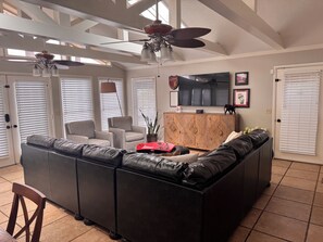A spacious living room with a sectional sofa, a television, and a ceiling fan.