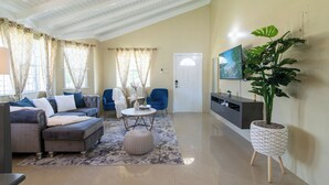A living room with a sectional sofa, a round coffee table, and a potted plant. - 15min to Ocho Rios-Family sized 2bed/2bath-Pool-BBQ Grill-100Mbps-Gated Complex (Drax Hall)