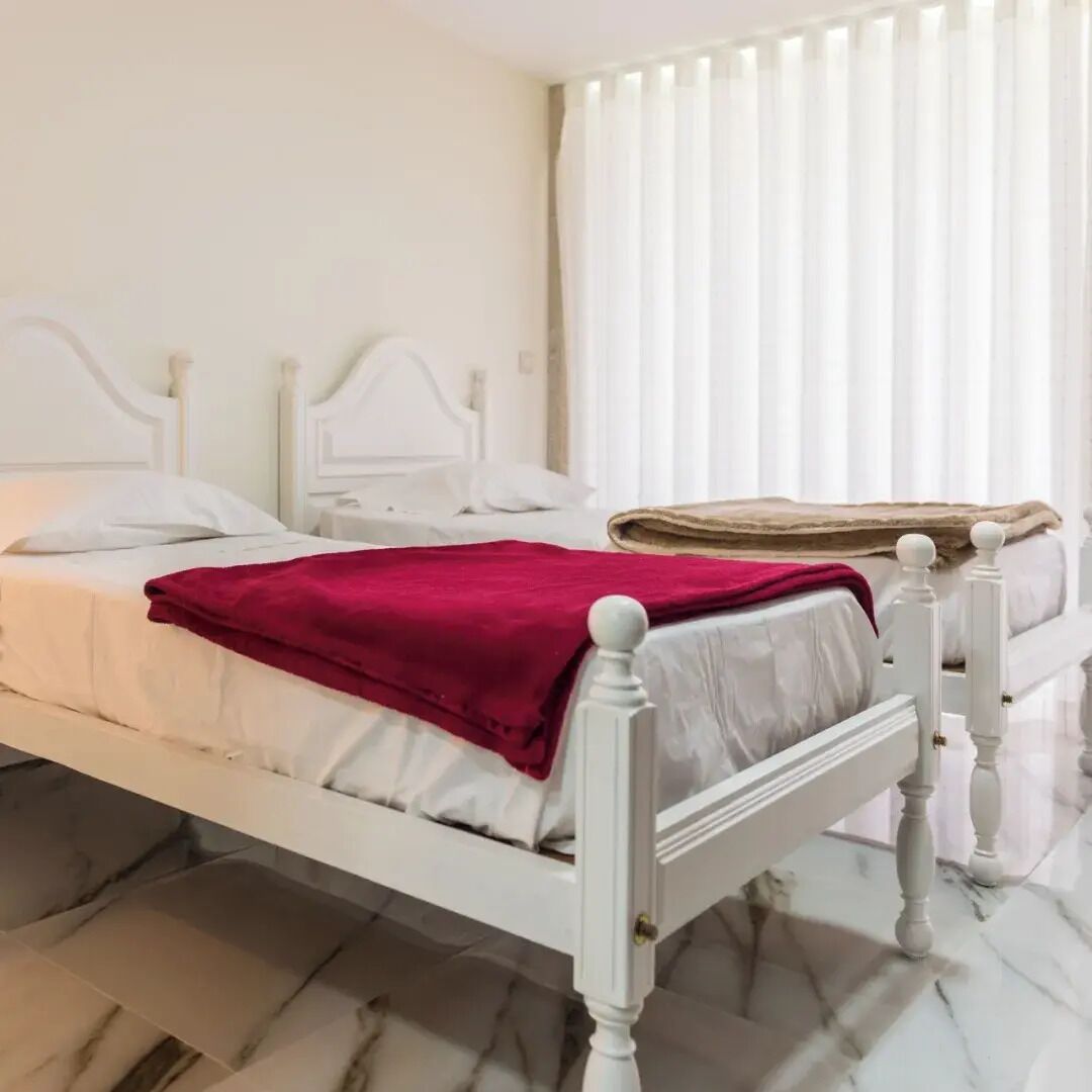 Un lit blanc avec une couverture rouge, une tête de lit blanche et un sol en marbre.