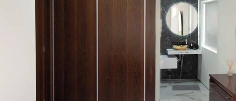 Un baño moderno con piso de mármol, un armario de madera, un lavamanos con encimera de mármol negro y un espejo grande.