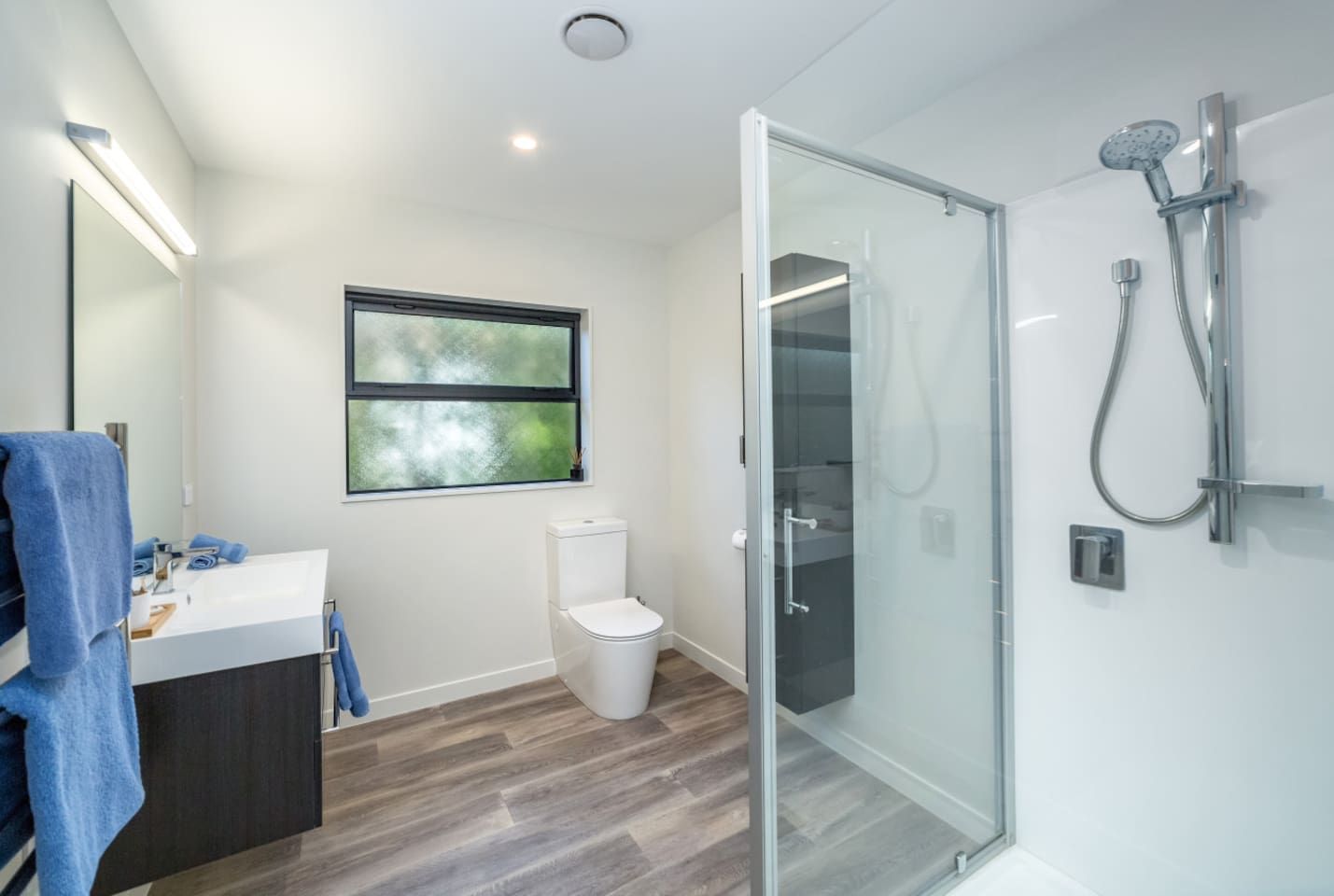 Un baño moderno con cabina de ducha de vidrio, inodoro y lavamanos con toallero.
