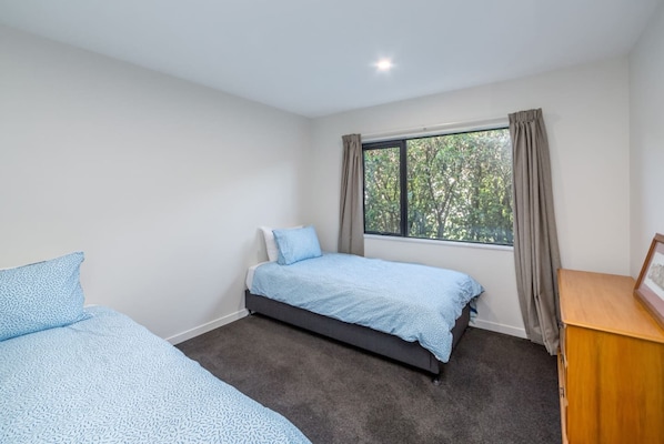 A bedroom with a single bed, a desk, and a window with curtains.