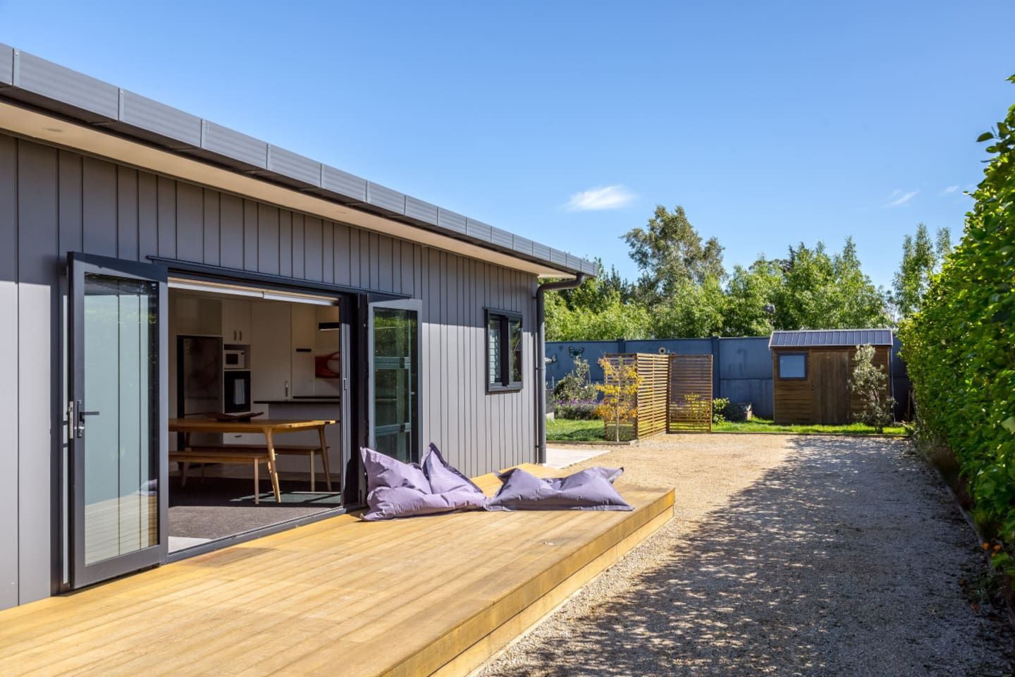 A modern house with a wooden deck, an open door leading to a kitchen, and a gravel driveway.
