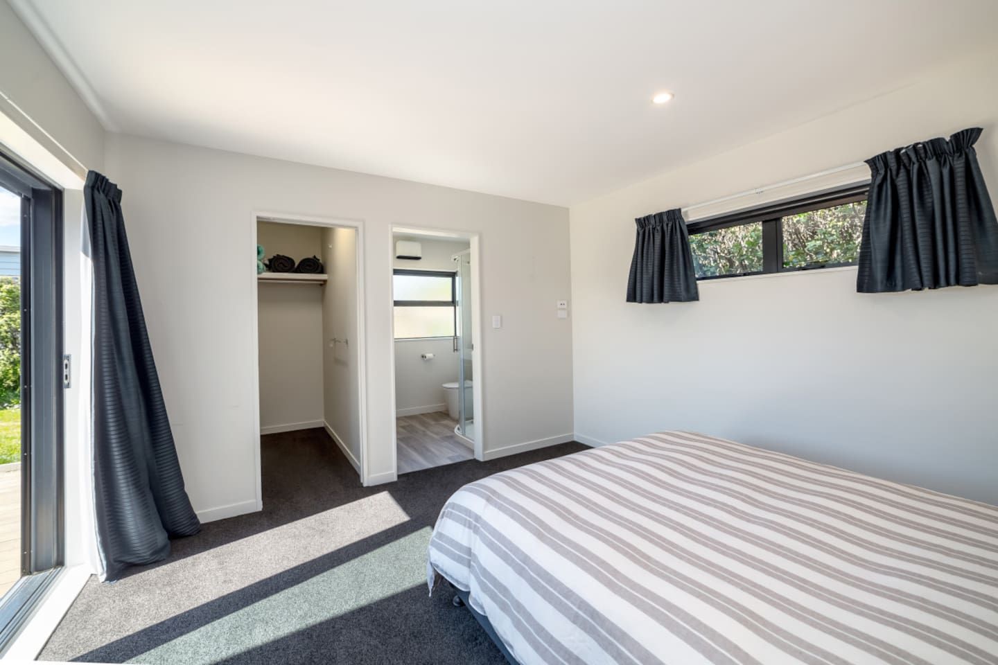 A bedroom with a bed, a window with curtains, a door leading to a bathroom, and a carpeted floor.