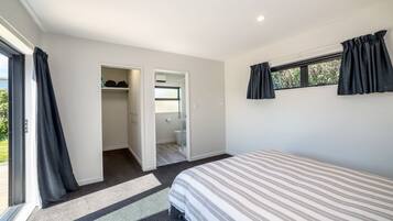 A bedroom with a bed, a window with curtains, a door leading to a bathroom, and a carpeted floor.