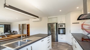 A modern kitchen with a central island, stainless steel appliances, and white cabinetry. - Private Escape – Seasonal Communal Pool, Tennis & Relaxed Living in Pinot Grove (Martinborough)