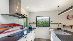 A modern kitchen with white cabinets, a black countertop, a stainless steel range hood, a window with a view of greenery, a clock on the wall, and a built-in sink. - Private Escape – Seasonal Communal Pool, Tennis & Relaxed Living in Pinot Grove (Martinborough)