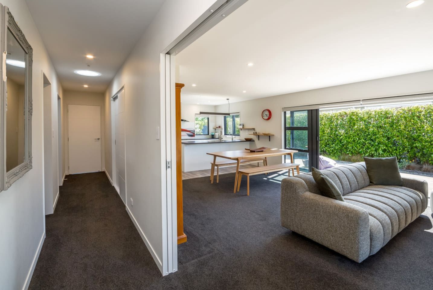 A modern interior with a dining area, a sofa, and a view of greenery outside.