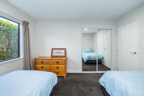 A bedroom with two beds, a dresser, a framed picture, and a sliding door leading to another room.