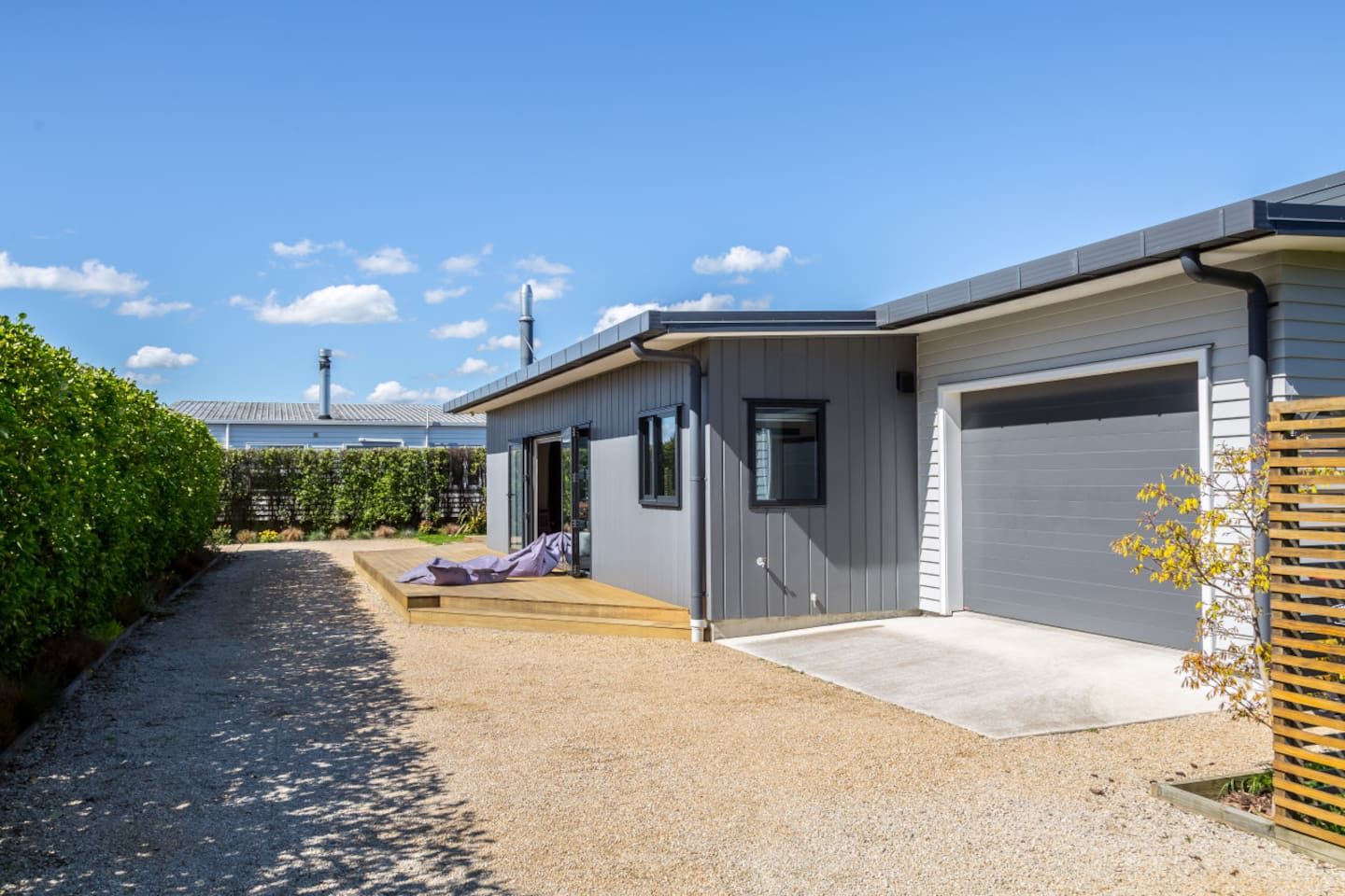A modern two-story building with a gravel driveway, a covered patio, and a garage.