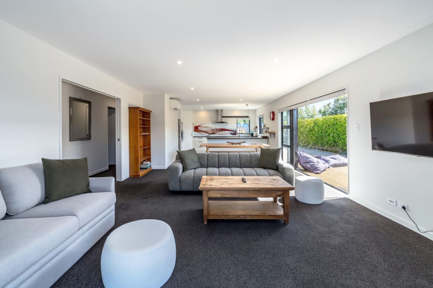 A modern living room with a grey sofa, a wooden coffee table, and a white ottoman.