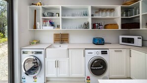 A laundry room with two washing machines, a sink, and shelves with various items.