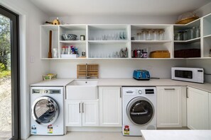 A laundry room with two washing machines, a sink, and shelves with various items.