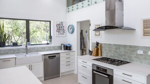A modern kitchen with white cabinetry, a built-in dishwasher, a stove, and a window with a view of greenery.