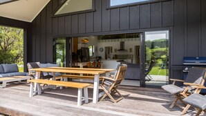Une terrasse extérieure avec des meubles en bois, un barbecue et une vue sur l’intérieur de la maison.