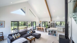 A spacious living area with a large sofa, a coffee table, and a dining area with chairs and a table. There is a kitchen with modern appliances and a large window.