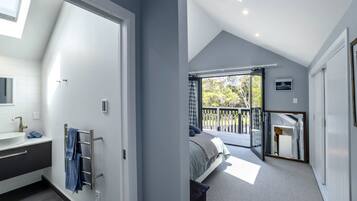 A modern bedroom with a large window, a balcony, and a bathroom with a sink and towel rack.