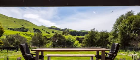 Un área de estar al aire libre con una mesa de picnic y sillas, con vistas a un paisaje verde con colinas y árboles.