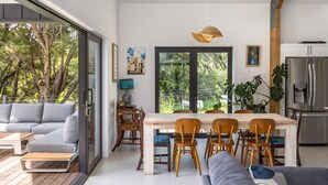 Une cuisine moderne avec une grande fenêtre, un coin repas avec des chaises en bois et un canapé gris.