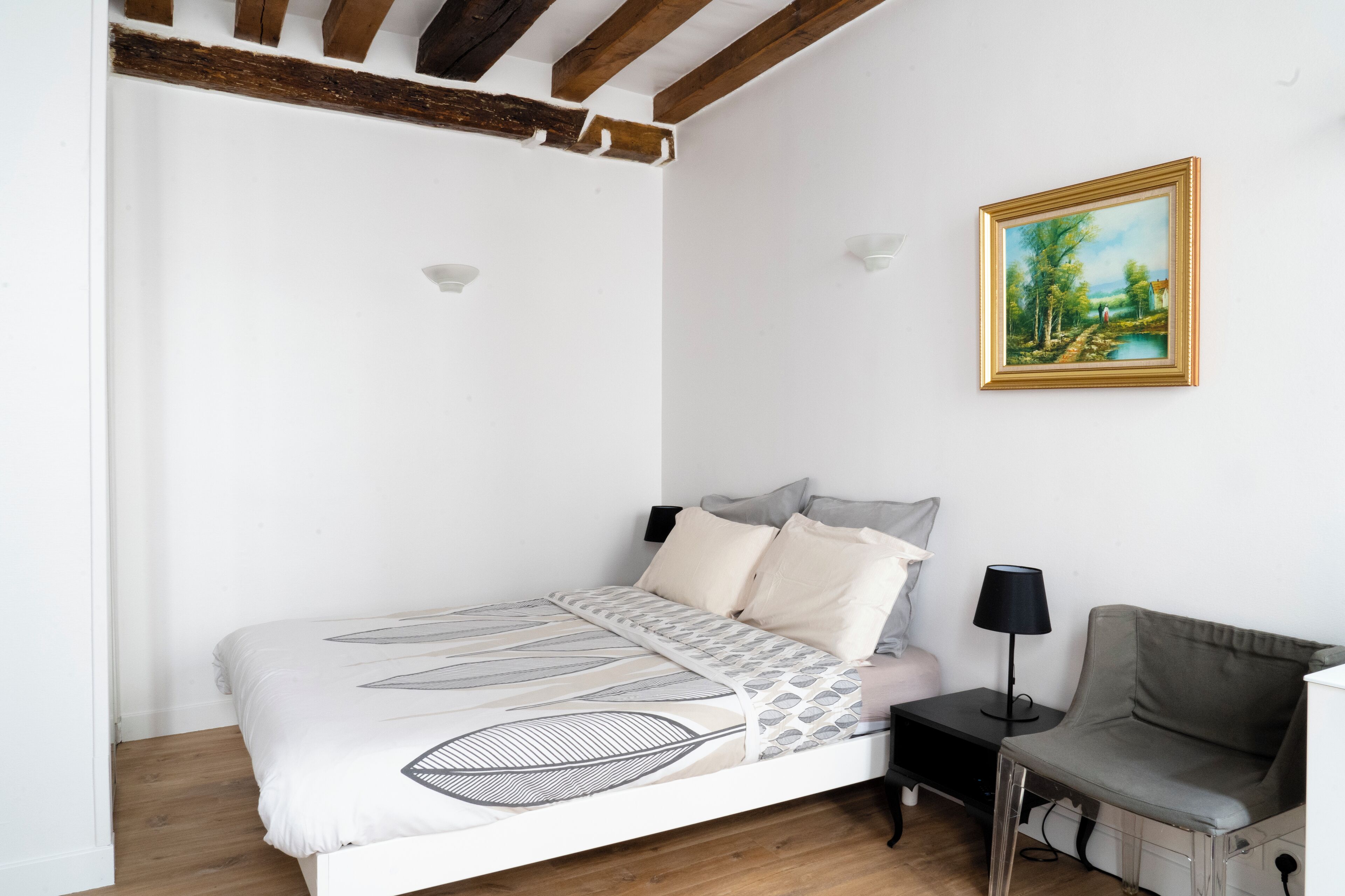 A bedroom with a bed, bedside table, lamp, and a painting on the wall.