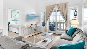 Una sala de estar moderna con un sofá, una mesa de centro y un televisor. Hay un balcón con vista a la playa.