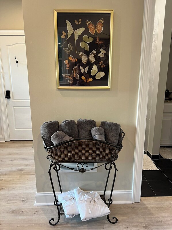 A room with a wicker bench holding towels, a framed butterfly artwork on the wall, and a white door in the background.