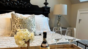 A neatly made bed with a wooden tray holding a bottle of Chianti Veroglio, two wine glasses, and a vase of flowers. - The Butterfly Suite exudes an air of timeless elegance and natural splendor. Named in homage to the myriad species of butterflies that adorn the surrounding landscape. (Jasper)