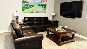 A living room with a black leather sofa, a wooden coffee table, and a flat-screen TV mounted on the wall. - Home Sweet Home (Fayetteville)