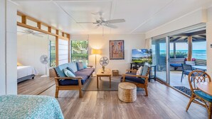 A spacious living area with a sofa, chairs, a coffee table, and a TV. There is a balcony with a view of the ocean.