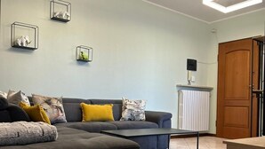 A living room with a dark grey sofa, a coffee table, and a wooden cabinet. There are three wall-mounted picture frames and a radiator on the wall.
