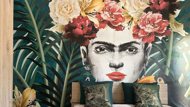 A bedroom with a large floral mural on the wall, a bed with teal bedding, and decorative pillows.