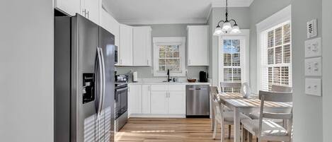 Una cocina moderna con armarios blancos, un refrigerador de acero inoxidable y una mesa de comedor de madera con sillas.