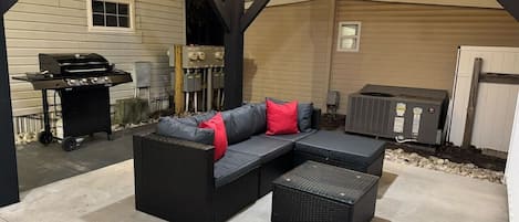 Un patio esterno con un divano componibile, un tavolino e un barbecue.