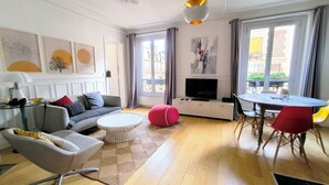 A modern living room with a sofa, coffee table, ottoman, TV, and dining area. - Cosy Parisian charm Paris 12e Montgallet  (Paris)