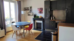 A modern kitchen with dark cabinets, a built-in oven, and a dining area with a round table and chairs. - Cosy Parisian charm Paris 12e Montgallet  (Paris)