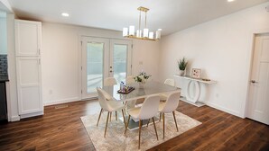 Een eetruimte met een glazen tafel, witte stoelen, een kroonluchter en een houten vloer.
