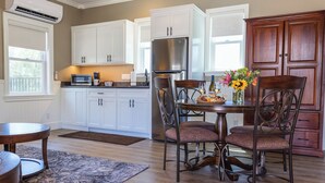 A kitchen with white cabinets, a stainless steel refrigerator, a dining table with chairs, and a window with blinds. - Bungalow #5 by Polo House and Bungalows (Santa Ynez)