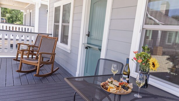 A covered porch with a table set for a meal, a rocking chair, and a door with a light blue door frame. - Bungalow #5 by Polo House and Bungalows (Santa Ynez)