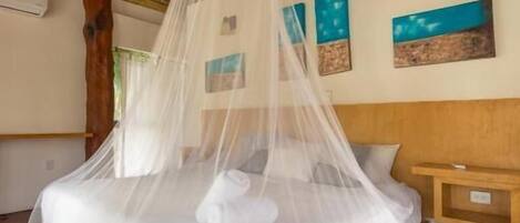 Una cama con mosquitero, cabecera de madera y mesita de noche con lámpara.