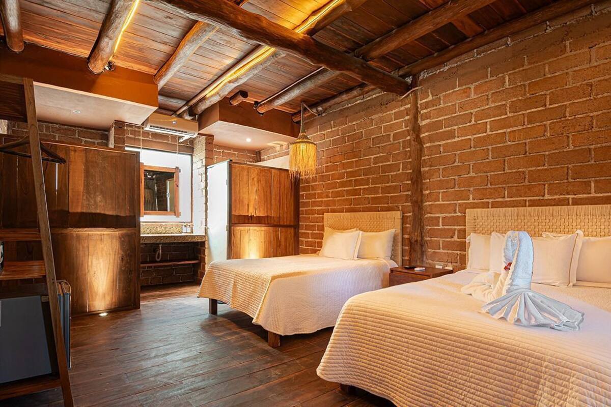 Una habitación de hotel rústica con dos camas, vigas de madera, paredes de ladrillo y una lámpara colgante.