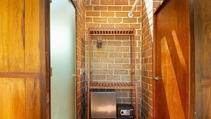 Ein kleiner, abgeschlossener Raum mit einer Backsteinwand, einer hölzernen Sitzbank, einem kleinen Kühlschrank und einem Radio.