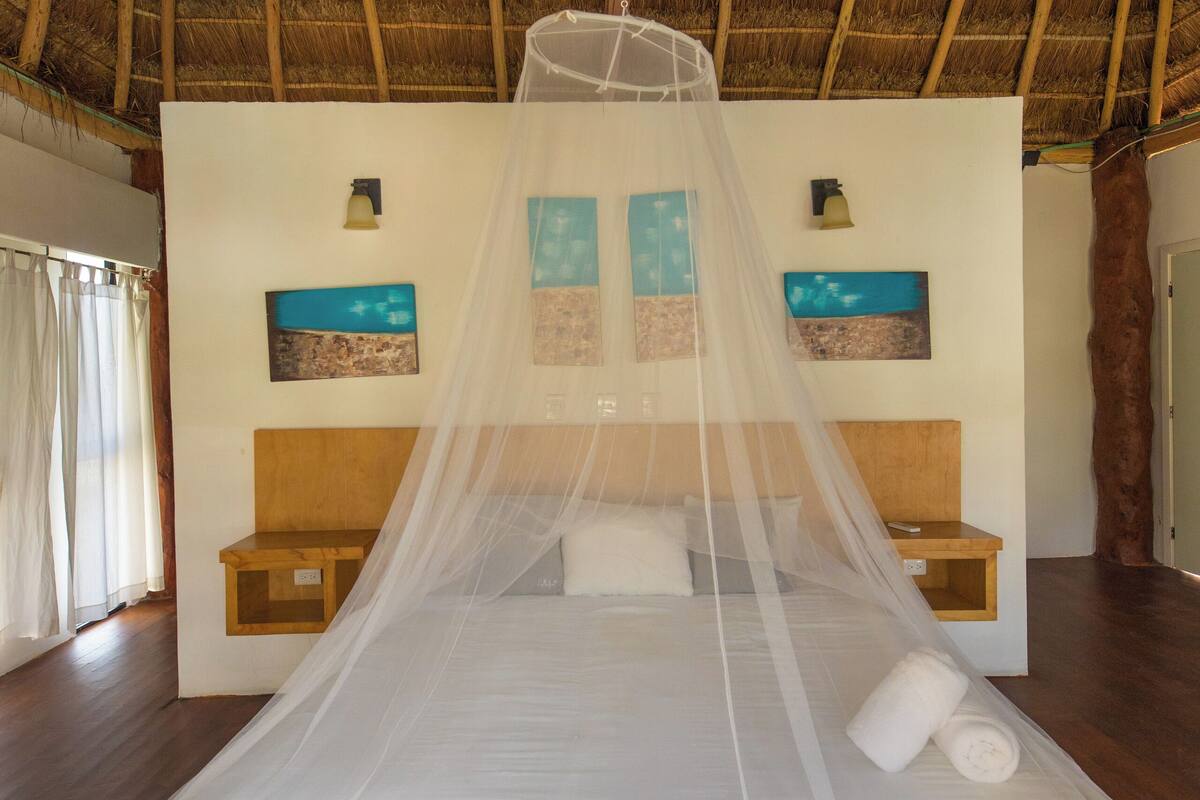 Una cama con mosquitero, cabecera de madera y mesita de noche con lámpara.