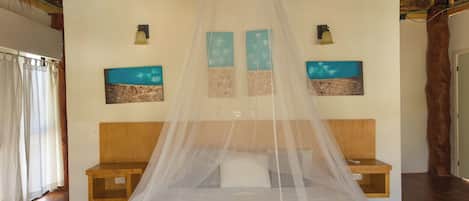 Una cama con mosquitero, cabecera de madera y mesita de noche con lámpara.