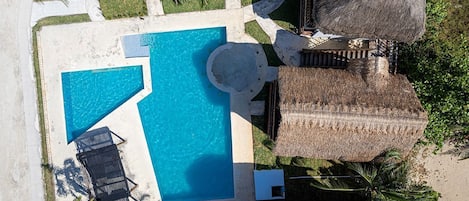 An aerial view of a resort with a central swimming pool, lounge chairs, and thatched-roof structures.