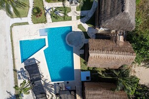 Vista aérea de un resort con piscina central, sillas de descanso y construcciones de techo de paja.