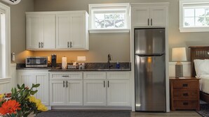 A kitchen with white cabinets, a stainless steel refrigerator, a microwave, and a coffee maker. There is a wooden table with a vase of flowers.