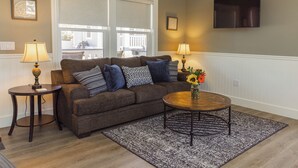 A living room with a sofa, two lamps, a coffee table with flowers, and a TV on the wall.