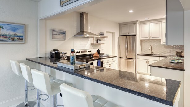 Una cocina moderna con una isla central, taburetes de bar, electrodomésticos de acero inoxidable y un letrero con temática playera.