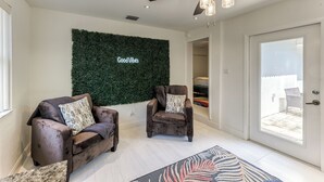 Una sala de estar moderna con dos sillones, un ventilador de techo y una pared verde con el texto 'Good Vibes'.