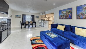 Una sala de estar moderna con un sofá azul, un tapete colorido y una cocina al fondo.